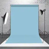 Light blue fabric backdrop with white brick wall and studio lighting setup.