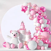Pink and white balloon arch with a teddy bear and decorative bottles.